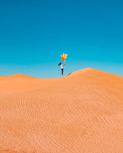 Man on sand dune in desert against clear blue sky