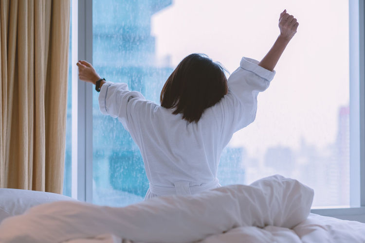 Rear view of woman with arms raised on bed