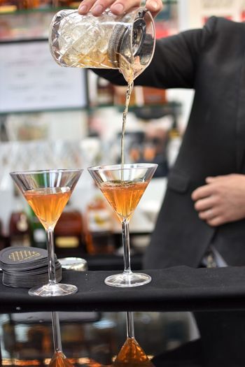 Midsection of bartender pouring cocktail in martini glass