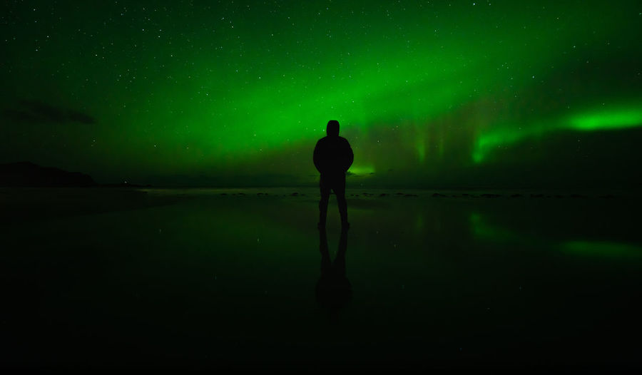 Rear view of silhouette man standing at beach against aurora borealis