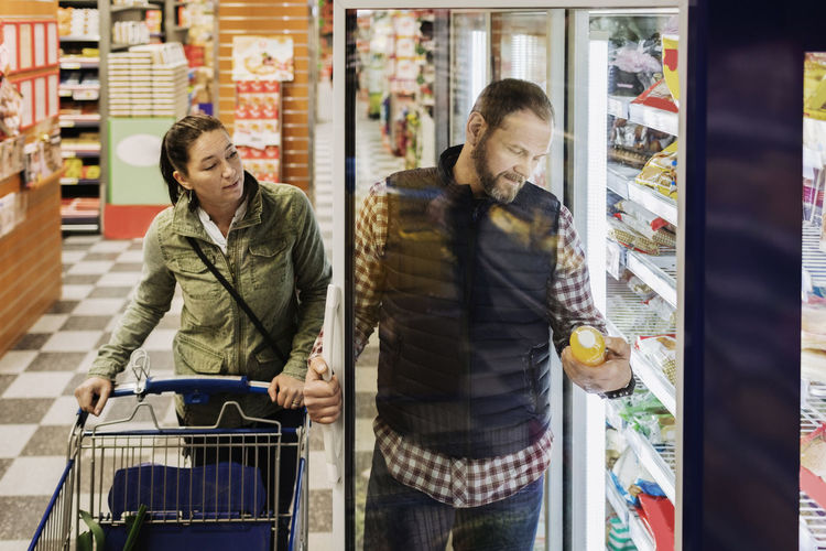 Couple buying groceries while standing by refrigerator in supermarket