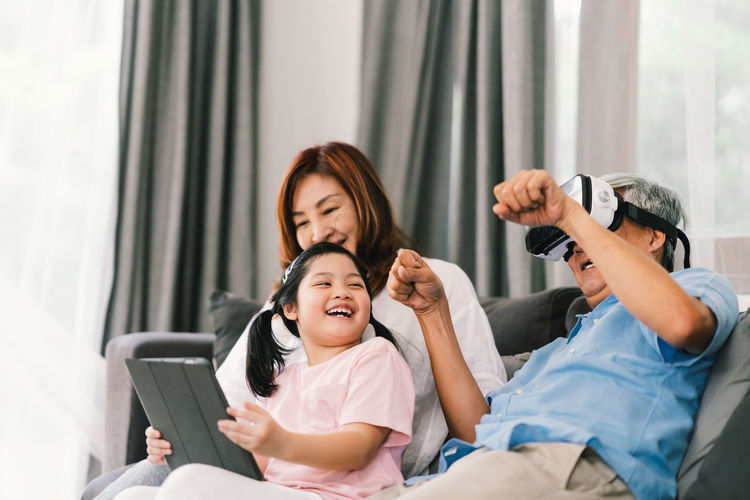 Smiling family using technologies while sitting on sofa