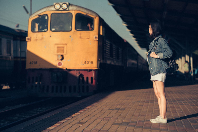 Full length side view of woman standing by train at railroad station