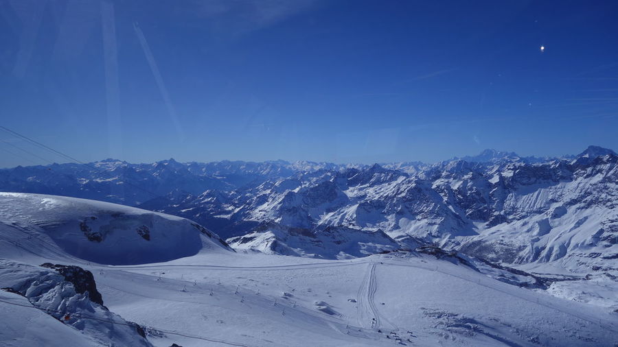Scenic view of snow covered mountains against blue sky