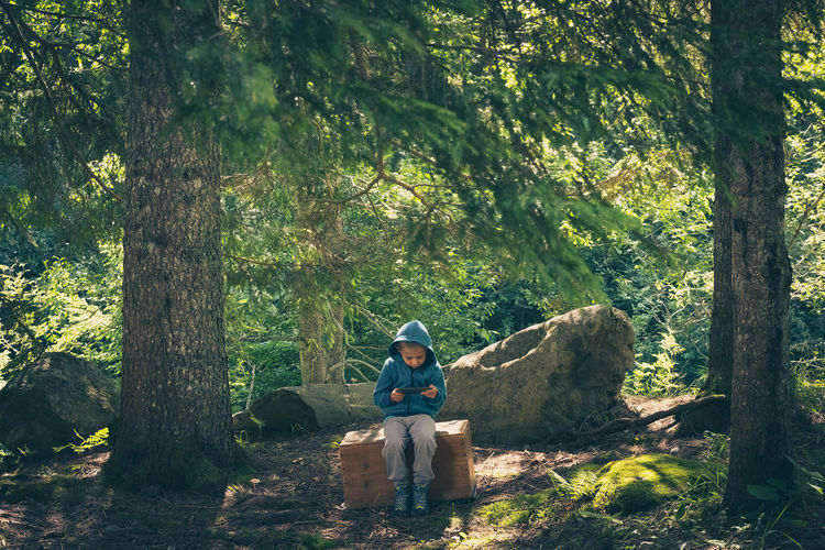 Portrait of boy sitting on tree trunk in forest