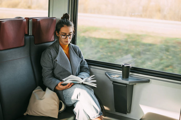 Young beautiful girl on a train reading a book while traveling in a train.