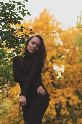Beautiful young woman standing against trees during autumn