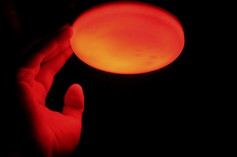 Cropped hand touching illuminated red light in darkroom
