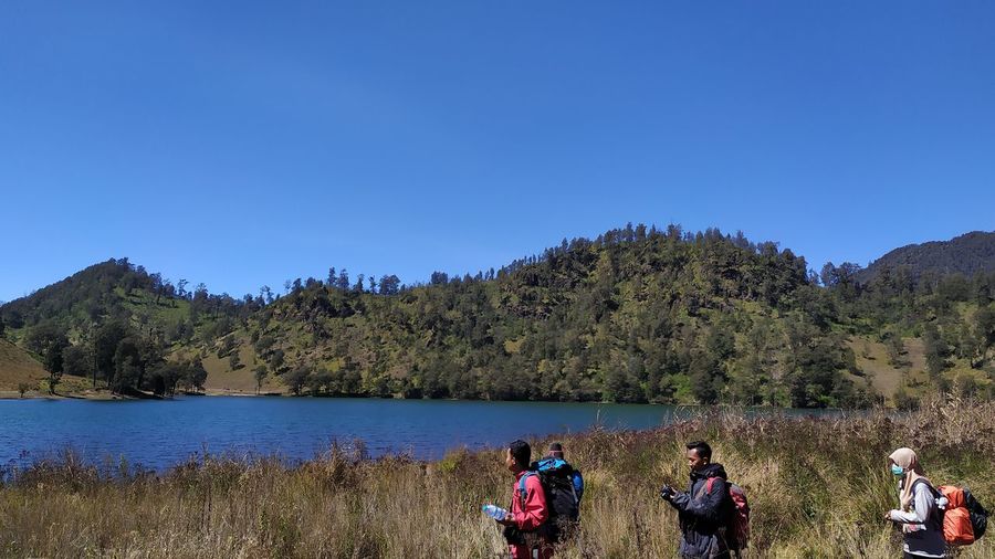 People on lake against clear blue sky