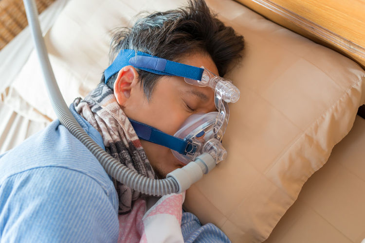 High angle view of mature man wearing oxygen mask while sleeping on bed