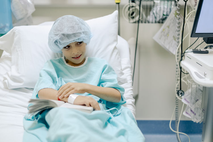 Smiling boy with hospital gown on bed with a book