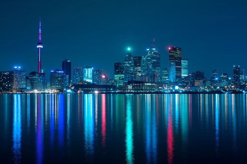 Illuminated skyscrapers by lake ontario against sky