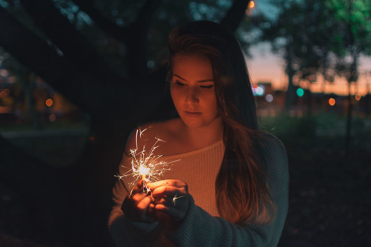Young woman holding illuminated sparkler at night