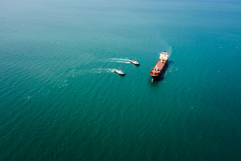 Red oil ship tank and tugboat sailing on green sea photograph aerial from drone point of view