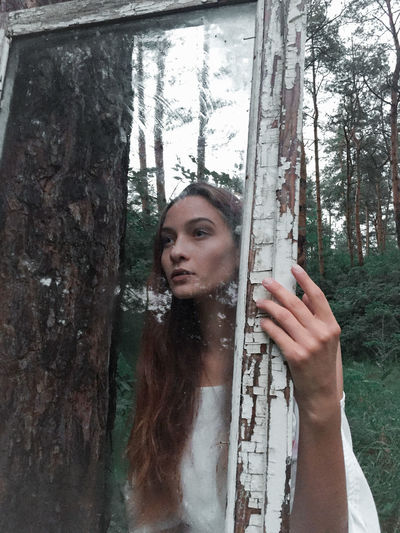Portrait of woman standing by tree trunk in forest