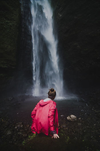 Woman sitting on rock against waterfall