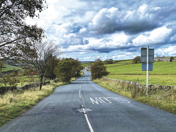Looking along the, denholme road, with trees, fields, and a cloudy sky near, leeming, keighley, uk