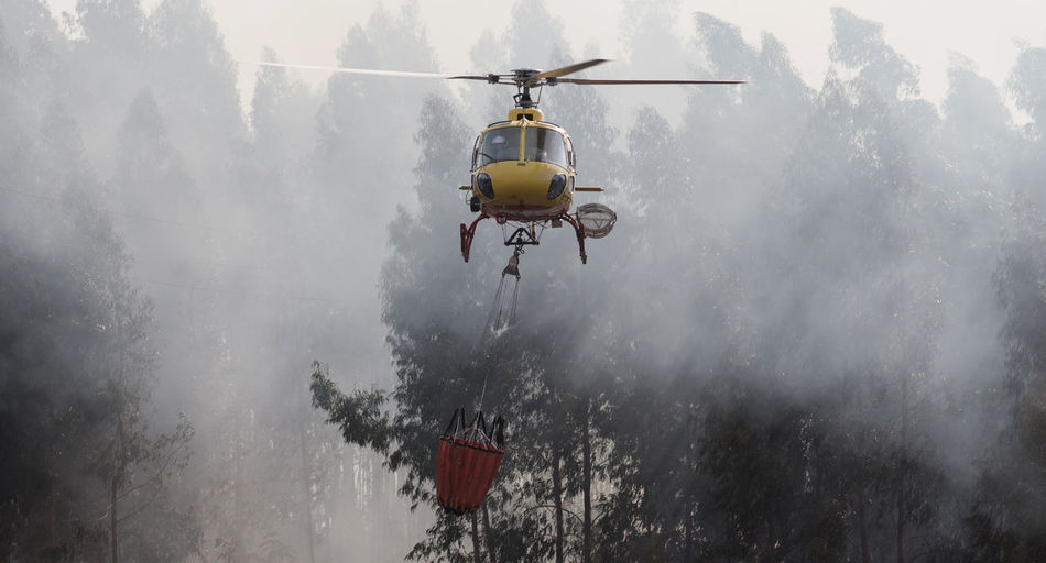 Firefighter helicopter fighting against a forest fire during day in braga, portugal.