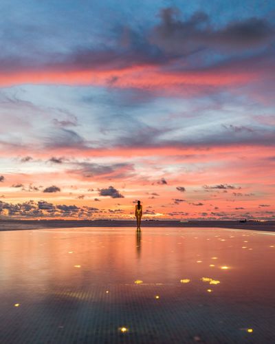 Distant view of woman standing in infinity pool against cloudy sky