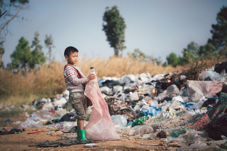 Full length of boy standing by garbage against sky