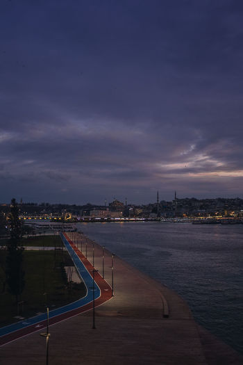High angle view of illuminated city by river against sky at dusk