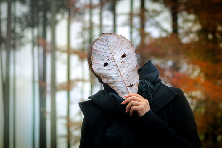Portrait of young woman holding leaf against face outdoors