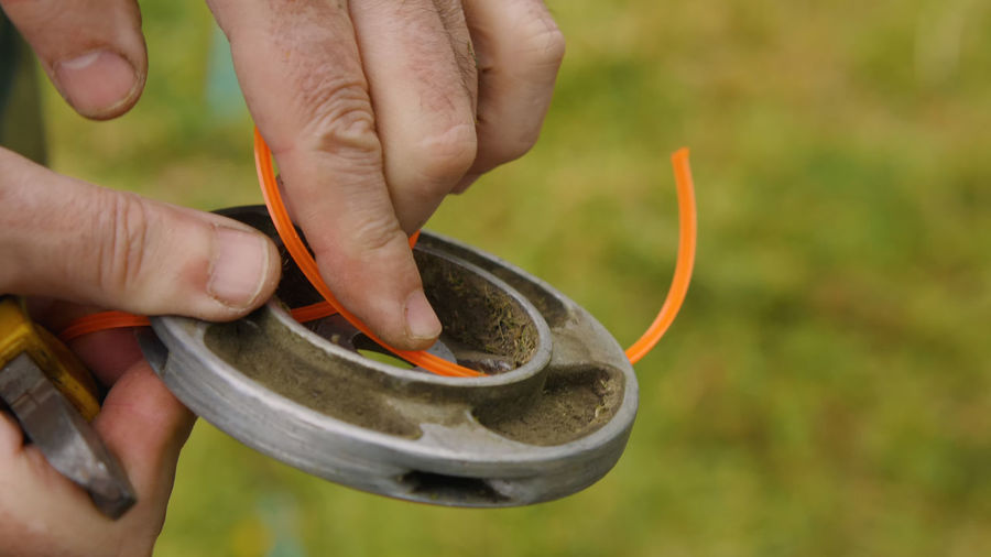 Close-up of a man's hands changing the line on the trimmer reel. installing a new orange line 