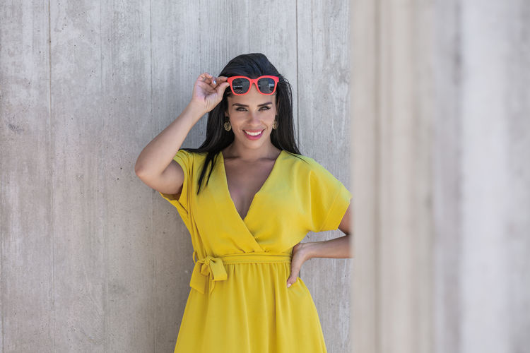 Woman in yellow dress wearing sunglasses and holding them on forehead looking at camera 