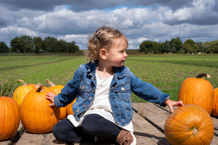 Full length of girl with pumpkins on field