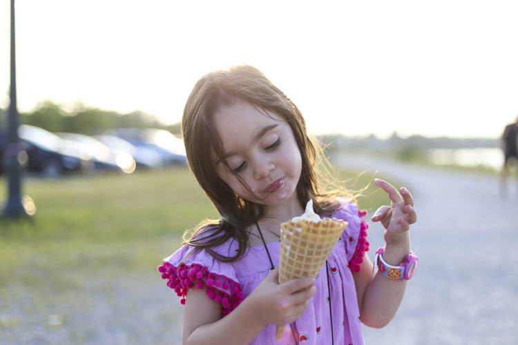 A little girl in a pink dress holding a big waffle cone