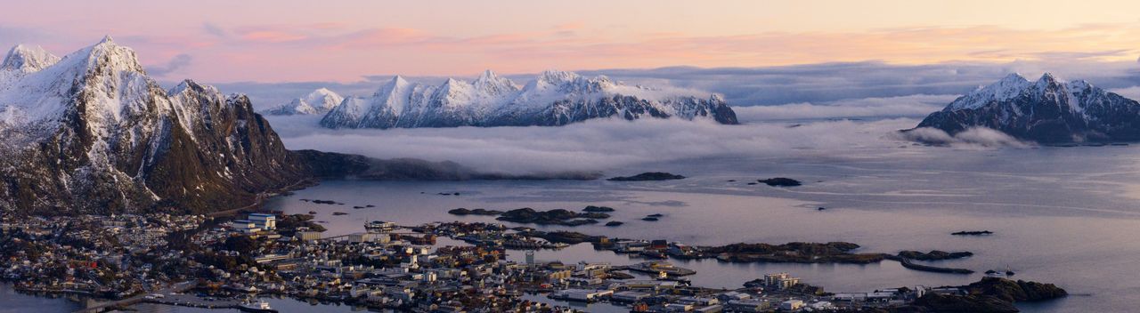 Scenic view of svolvaer and snowcapped mountains against sky during sunset