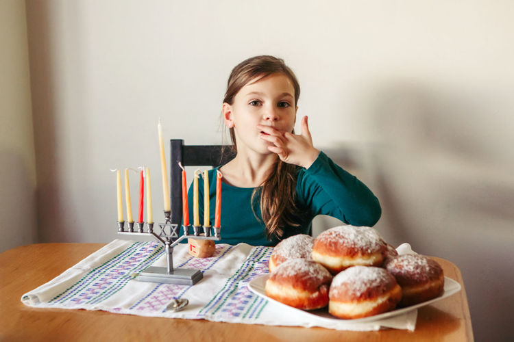 Kid eating sufganiyot donuts, sweet festive food. girl with menorah for a jewish hanukkah holiday 