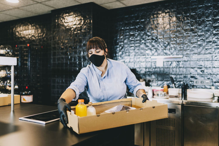 Female chef carrying cardboard box at counter in restaurant kitchen