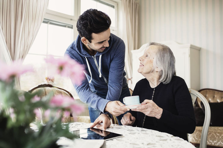 Happy caretaker serving coffee to senior woman in nursing home