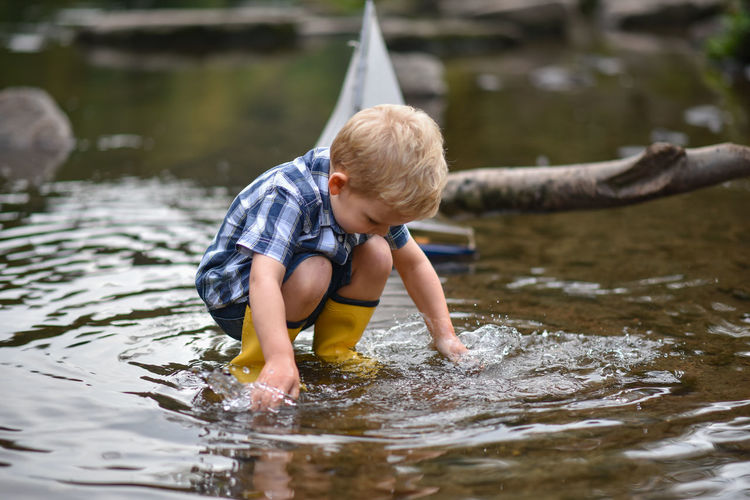 Child, little boy is playing in the water with a boat.