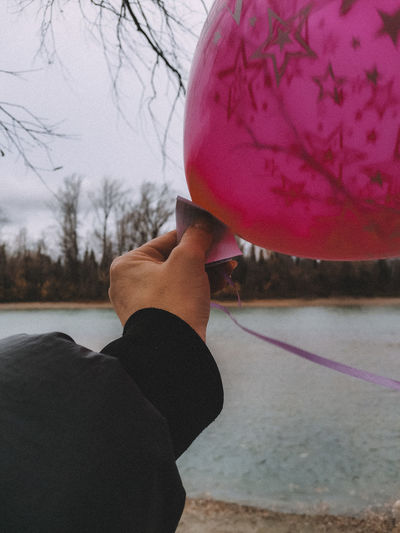 Midsection of person holding balloons at lake against sky
