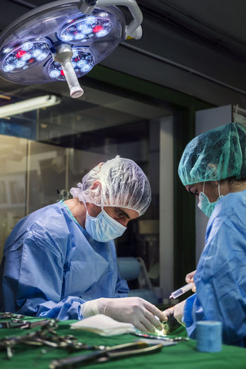 Side view of focused vet doctor with assistant in uniform and medical mask performing surgery in operating room in modern clinic