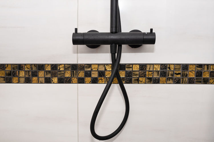Black metal shower tap with temperature control, covered with a delicate white water stone.