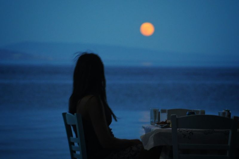 Side view of woman looking at sea against sky during dusk