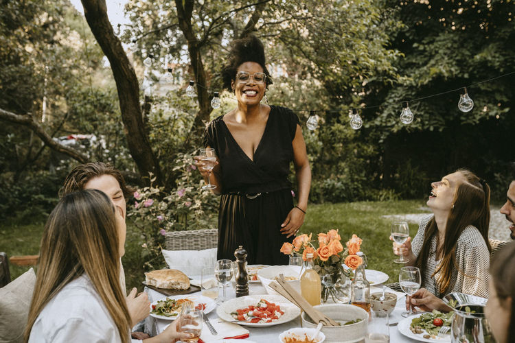Cheerful woman talking to friends by table during garden party