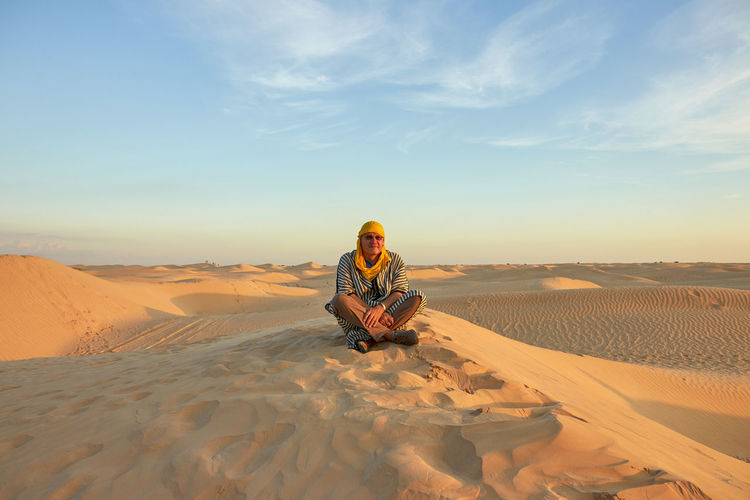 Man sitting on sand dune in desert against sky