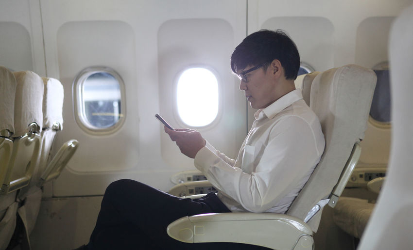 Midsection of man using mobile phone while sitting in airplane