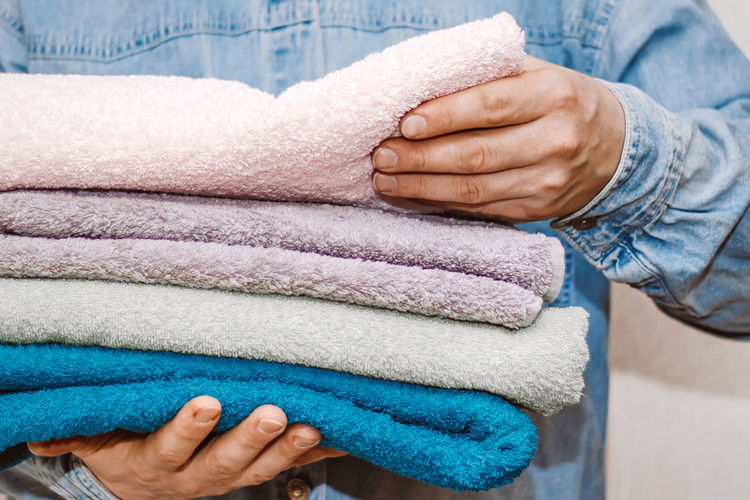 Man holds stack of fresh terry towels. organization and cleaning of house. storage and housekeeping