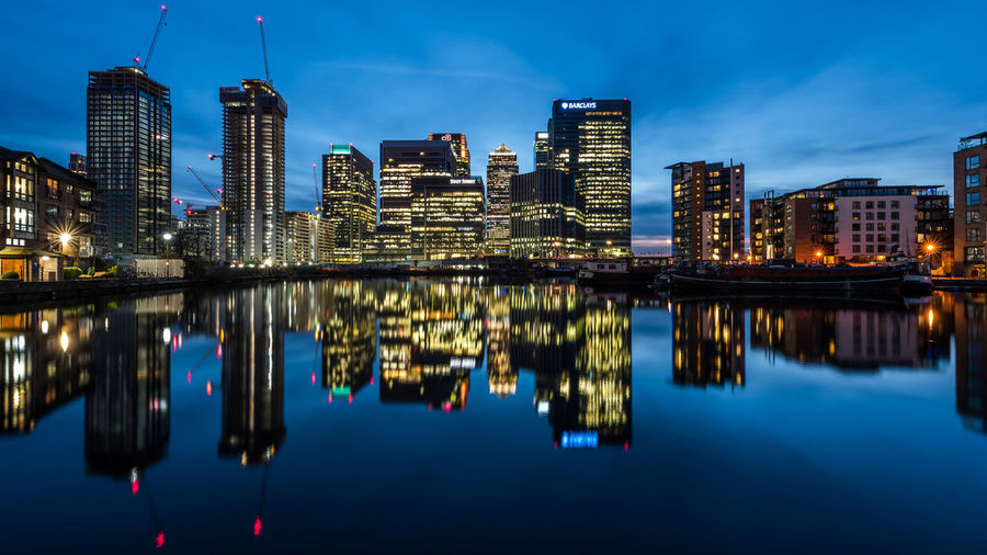 Reflection of illuminated buildings in river against blue sky