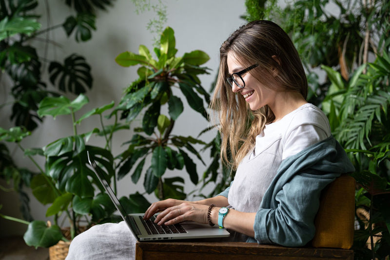 Young woman using laptop by plants