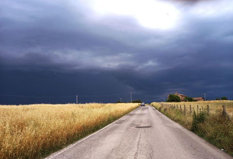 Strada fra i campi di grano e il cielo carico di tempesta 