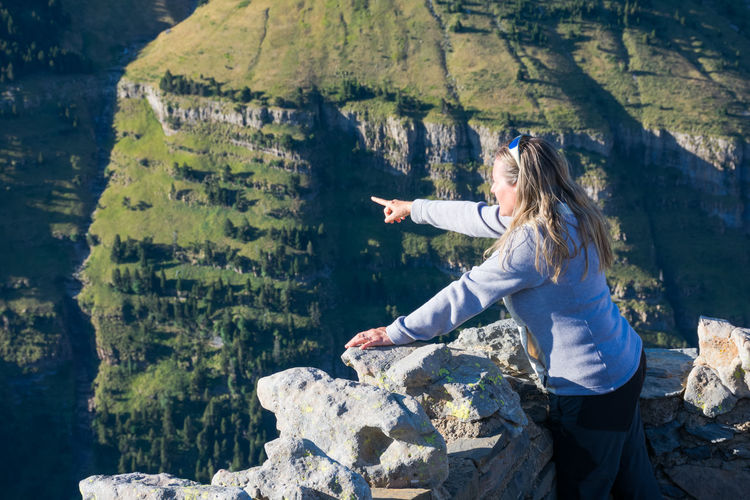 One woman pointing with her finger at a place of ordesa national park. she is admiring from the top of a balcony mountain the whole valley, the green forests, the rocks and the hills horizont