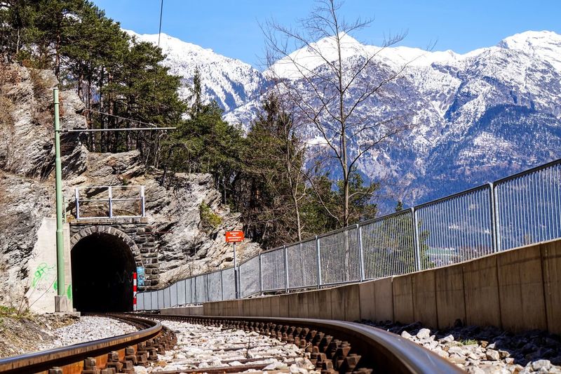 Railroad tracks leading towards tunnel against snowcapped mountains