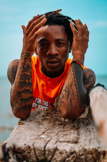 Portrait of young man with tattoos at the beach against sky