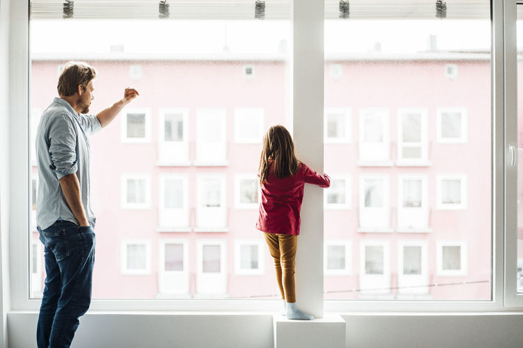 Daughter and father standing by window at home